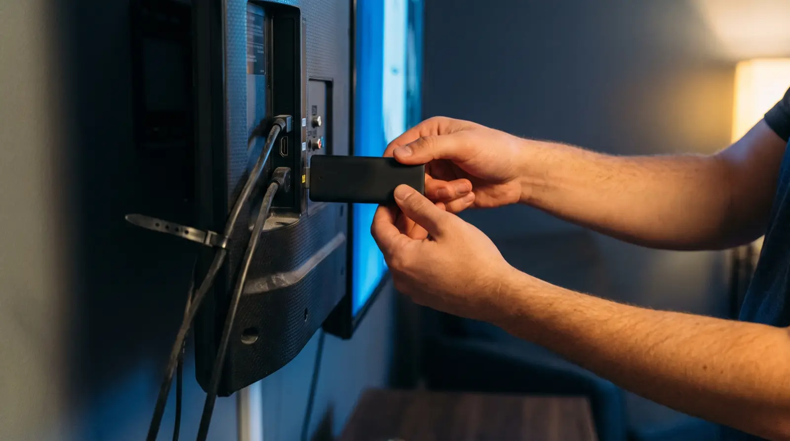 Handen sluiten een streaming-stick aan op de HDMI-poort achter een televisie