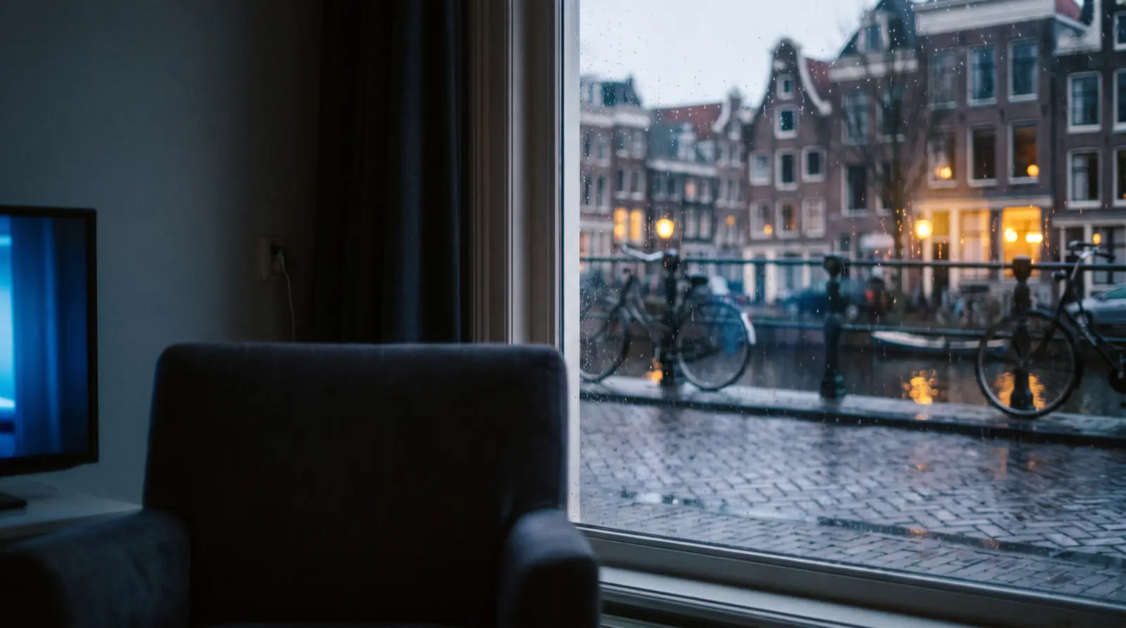 Woonkamer aan een Amsterdamse gracht met de televisie aan en regen op de ruit